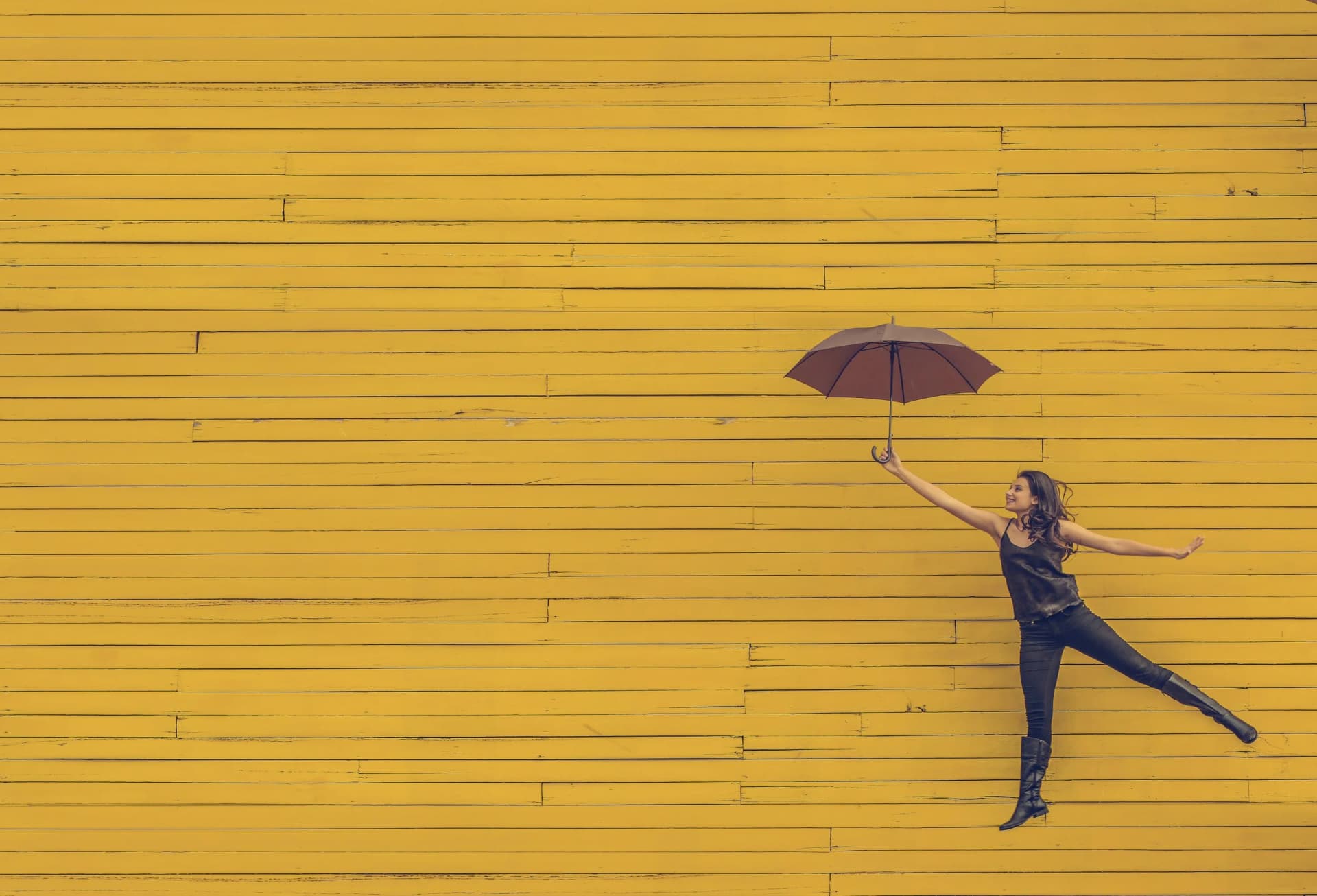 Woman with umbrella against yellow wall